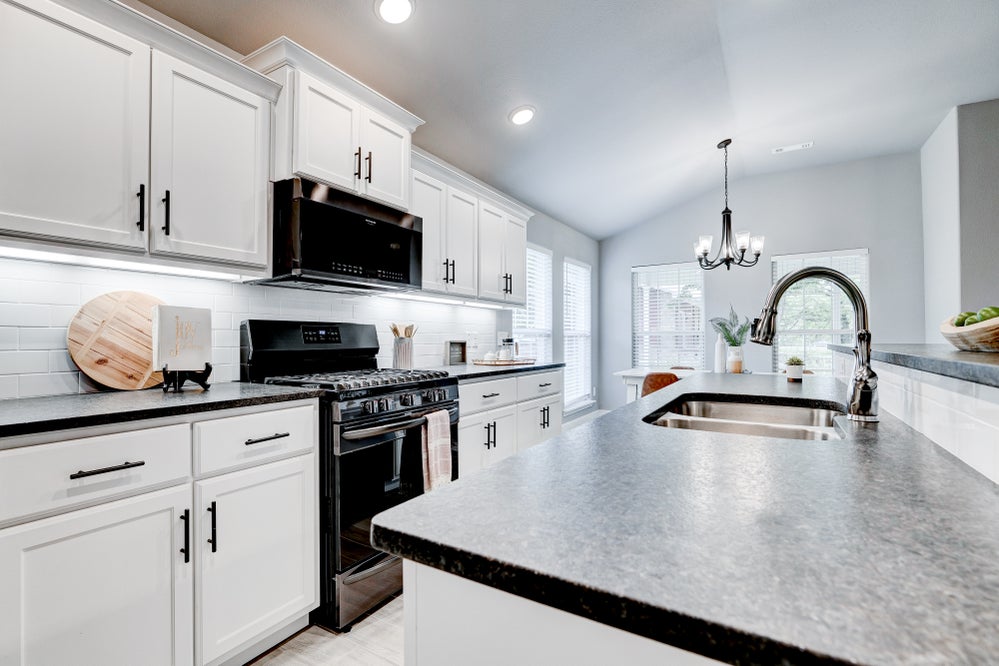Side view of black granite counters and white cabinets kitchen with dining nook in the distance