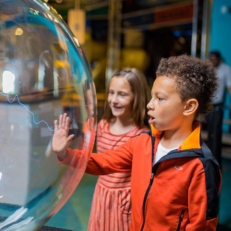 a kid with his hand against a glass globe with a line of electricity meeting his hand