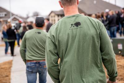 the backs of two men in green long sleeve t-shirts with the schuber mitchell logo and #lovecominghome