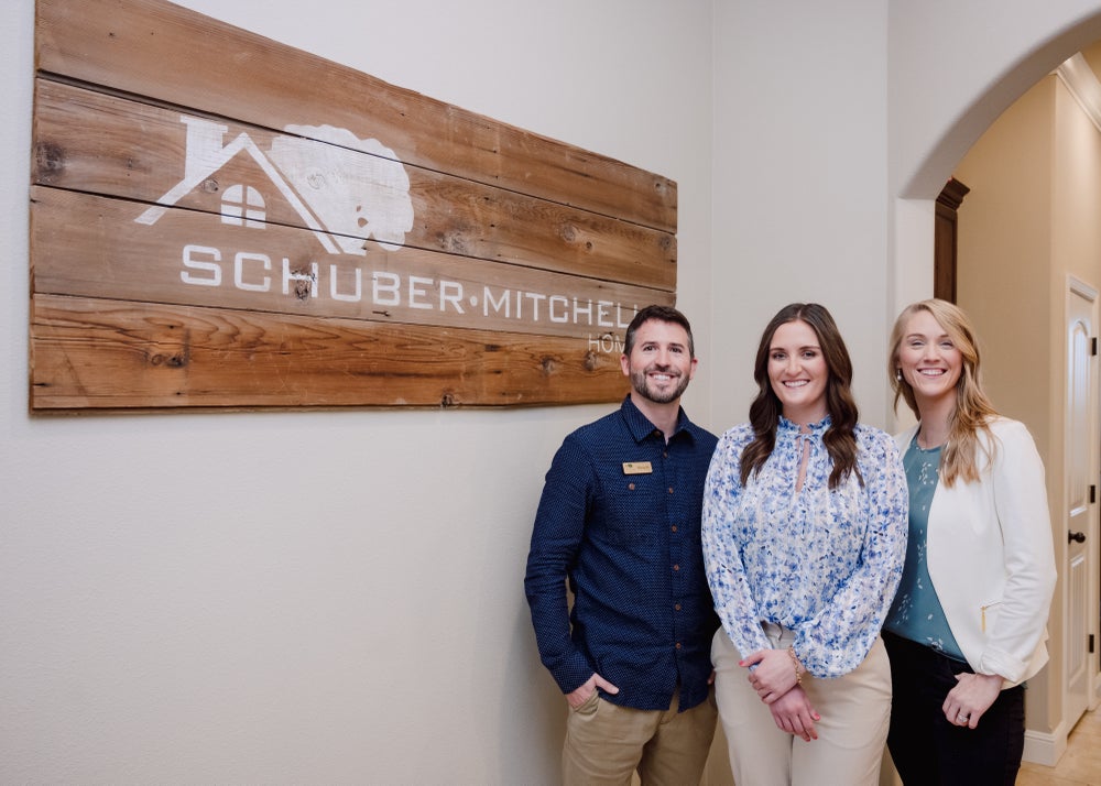 Three members of our sales team standing next to the Schuber Mitchell Homes logo