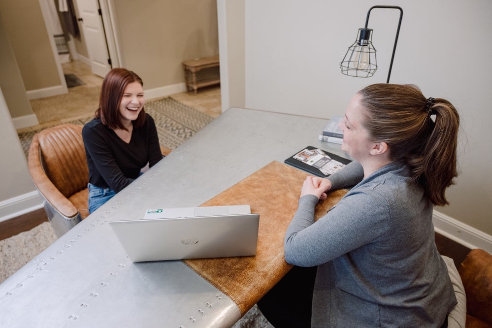 Two ladies laughing while sitting at a desk discussing financing options