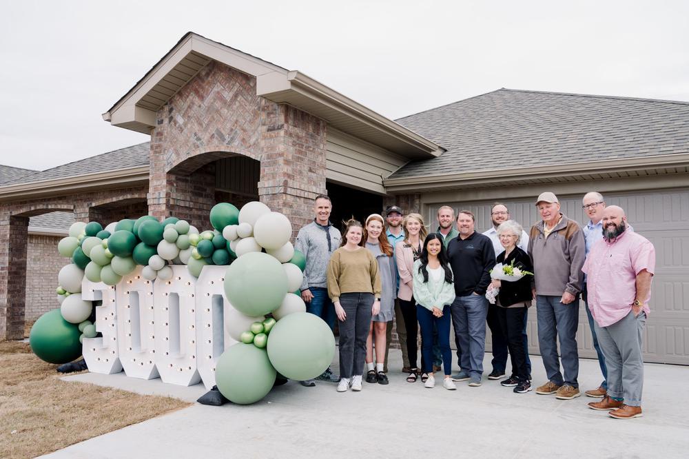 a group of people standing in front of a new home with the numbers 3000 in light up marquee letters and a green balloon arch