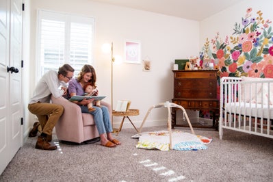 Mom and Dad reading a book to their little one in the nursery, flower mural painted on one of the walls